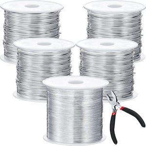 May include: Five spools of silver-colored wire are stacked on white spools. A pair of black and red handled pliers rests on the bottom spool. The wire is tightly wound, and the spools are arranged in a visually appealing manner.