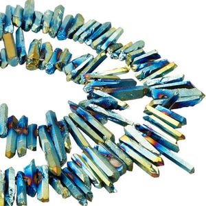May include: A strand of raw, elongated crystal points featuring an iridescent finish with vibrant shades of metallic blue, teal, and gold. Each individual stone is faceted and strung together, displaying a reflective, multi-colored surface.
