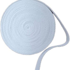 May include: A roll of light blue elastic ribbon. The ribbon is tightly wound in a circular shape, with a portion of the ribbon extending outwards. The texture of the ribbon appears slightly textured.