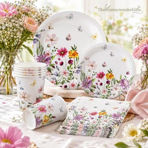 May include: A set of white disposable party supplies featuring a colorful floral and butterfly print. The collection includes two sizes of round plates, a stack of paper cups, and a stack of folded paper napkins, all decorated with wildflowers.
