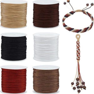May include: Spools of cord in various colors, including tan, brown, black, white, and red. A macrame bracelet and a tassel with beads are also shown. The cord is likely used for crafting and jewelry making.