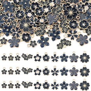 May include: A collection of metal flower charms featuring black enamel petals with gold-toned edges. Some charms include small clear rhinestones at the center. The charms are arranged in a large pile at the top and in three organized rows below.