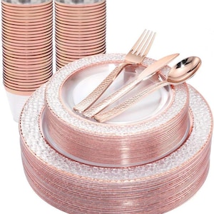 May include: A rose gold disposable tableware set, including plates, cups, and cutlery. The plates have a textured, decorative border. The cutlery includes forks, knives, and spoons. The cups and plates are stacked, and the cutlery is arranged on top of the plates.
