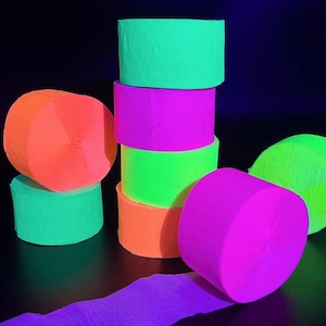 May include: A stack of neon colored crepe paper streamers in orange, green, pink, and purple. The streamers are rolled up and ready to be used for party decorations.