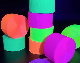 May include: A stack of neon colored crepe paper streamers in orange, green, pink, and purple. The streamers are rolled up and ready to be used for party decorations.