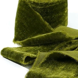 May include: A roll of olive green velvet ribbon with a soft, textured surface. The ribbon is unrolled in sections, revealing the fabric's plush texture and color. The edges are slightly frayed.