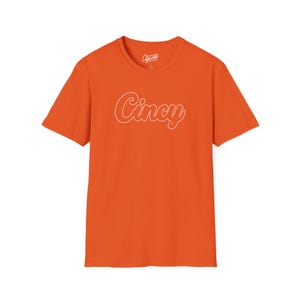 Puede incluir: Camiseta naranja de manga corta con un contorno blanco de la palabra "Cincy" en la parte delantera.