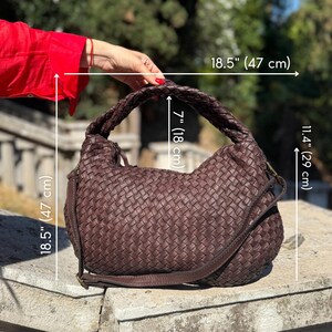 May include: A brown woven leather handbag with a braided handle and a shoulder strap. The bag is 18.5 inches (47 cm) wide, 11.4 inches (29 cm) high, and the handle is 7 inches (18 cm) high.