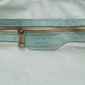 May include: Close-up of a light blue leather bag with a brass zipper and pull. The label reads "VERA PELLE MADE IN ITALY". The bag's interior is a matching light blue color.