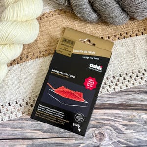 May include: A white ceramic mug with a black handle and the text "But First, Coffee" in a bold, black font. The mug is set against a blurred background, suggesting a cozy setting.