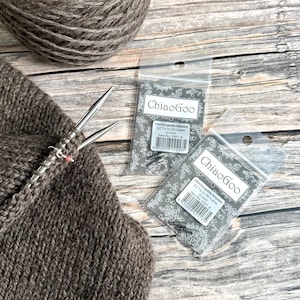 May include: Image of knitting supplies. Two packets of ChiaoGoo interchangeable adapters, a ball of yarn, and a partially knitted item. The packets have the text "ChiaoGoo" and "Interchangeable Adapters". The yarn and knitted item are brown.