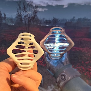 Puede incluir: Un modelo impreso en 3D de un objeto blanco, geom&eacute;trico, parecido a una jaula. El objeto est&aacute; en la mano de una persona. En el fondo, se muestra un objeto similar en un videojuego.