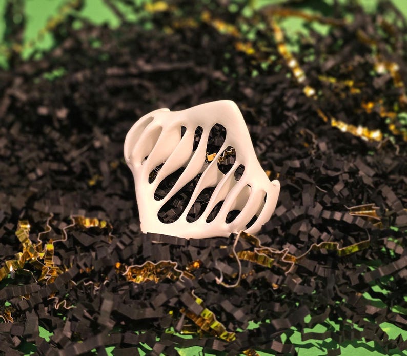 Puede incluir: Objeto decorativo de pl&aacute;stico blanco con un dise&ntilde;o geom&eacute;trico calado. El objeto est&aacute; sentado en una cama de papel triturado negro y dorado.