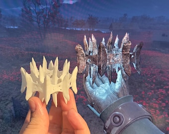 Op de afbeelding: Twee 3D-geprinte kronen, een witte en een zilveren, met een stekelig ontwerp. De kronen worden getoond tegen de achtergrond van een videogamelandschap.