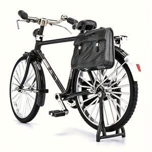 May include: A black bicycle model with a leather saddlebag. The bicycle has silver handlebars, wheels, and a kickstand. The tires are black, and the frame is black. The bicycle is a miniature replica.
