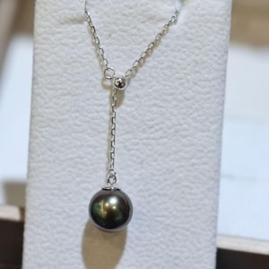 May include: A silver-toned necklace featuring a delicate chain and a single, round, dark gray pearl pendant. The chain passes through a small, polished silver-toned bead, creating a Y-shaped drop design with the pearl suspended at the bottom.