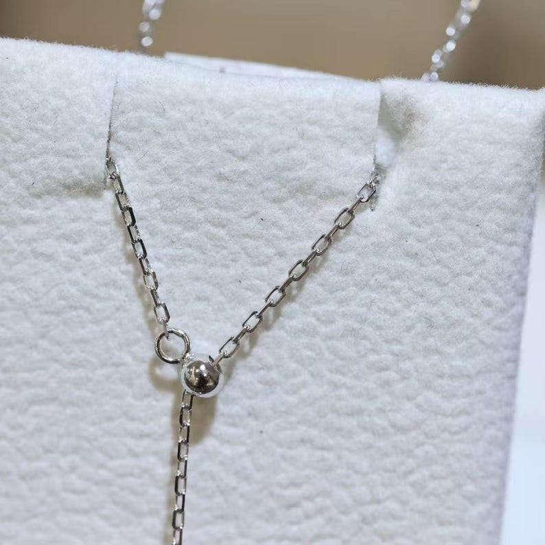 May include: A silver-toned necklace chain featuring a delicate link design and a small, round, sliding adjustable bead mechanism. The metallic chain is thin and polished, with the adjustable bead positioned to allow for length customization.
