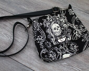 May include: Black and white skull and floral print crossbody bag with a black adjustable strap.