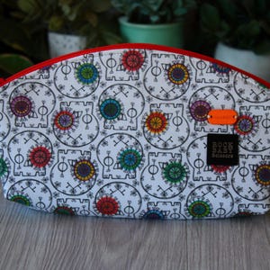 May include: White cosmetic bag with a repeating pattern of black skulls and colorful floral designs. The bag has a red zipper and a small orange tag. The text "ROCK BABY Scissors" is printed on a black tag.