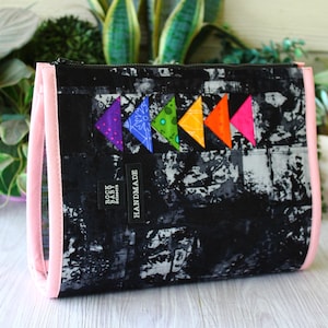 May include: A rectangular zippered pouch featuring a black and white abstract print with a row of five colorful triangular fabric accents in purple, blue, green, orange, and pink. A black label reads ROCK BABY SCISSORS and HANDMADE in white text.