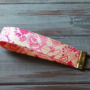 May include: A white fabric strap with a pink and white pattern. The strap has a gold metal buckle.