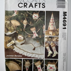 May include: McCall's Crafts M4691 sewing pattern envelope featuring Joanne Beretta designs. The front shows embroidered Christmas ornaments, stockings, a tree skirt, and a cone-shaped tree decoration with floral motifs and gold fringe accents.