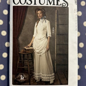 May include: McCall's Costumes sewing pattern featuring a historical dress design. The pattern includes a white blouse, skirt, and apron. The image shows a woman wearing the costume. The pattern is designed and printed in the USA.