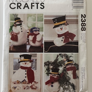 May include: A McCall's Crafts 2388 sewing pattern envelope featuring illustrations of various snowman-themed projects. The designs include plush snowmen wearing black top hats and red scarves, a snowman stocking, and a snowman wall pocket organizer.
