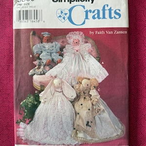 May include: A Simplicity Crafts sewing pattern envelope 9360 by Faith Van Zanten featuring illustrations of four stuffed animal dolls in various outfits, including a blue suit, a white lace dress, a long white lace gown, and a tan dress.