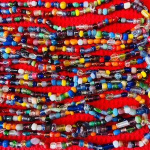 May include: A collection of multi-colored glass beads arranged in horizontal rows. The beads feature various shapes and sizes, including translucent, opaque, and clear finishes in shades of blue, yellow, green, red, orange, and white.