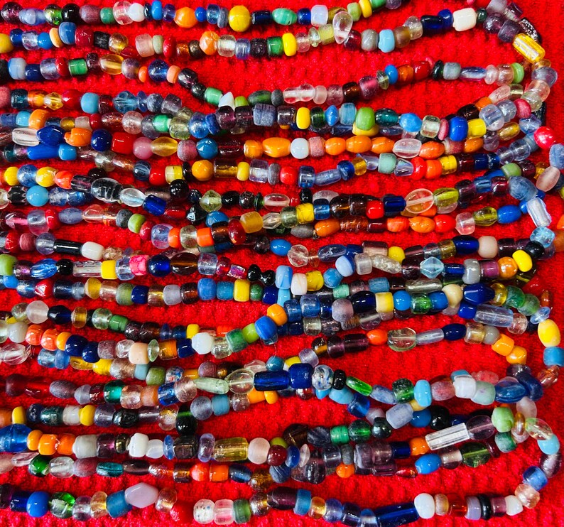 May include: A collection of multi-colored glass beads arranged in horizontal rows. The beads feature various shapes and sizes, including translucent, opaque, and clear finishes in shades of blue, yellow, green, red, orange, and white.
