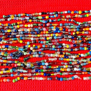May include: A long strand of multi-colored glass beads featuring a variety of shapes, sizes, and hues including blue, yellow, green, red, and clear glass. The beads are strung together in a continuous line, creating a vibrant and textured accessory.