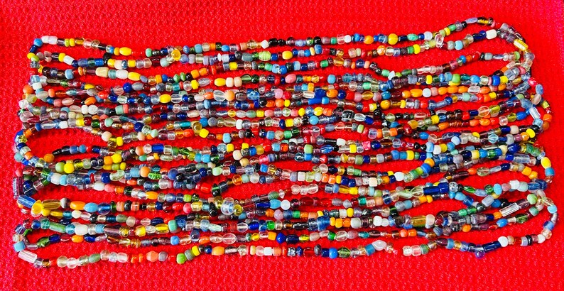 May include: A long strand of multi-colored glass beads featuring a variety of shapes, sizes, and hues including blue, yellow, green, red, and clear glass. The beads are strung together in a continuous line, creating a vibrant and textured accessory.