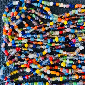 May include: A collection of multi-colored glass beads strung together in multiple strands. The beads feature a variety of shapes and sizes, including translucent, opaque, and clear glass in shades of blue, red, yellow, green, orange, and purple.