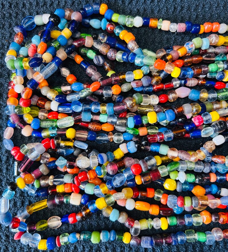 May include: A collection of multi-colored glass beads strung together in multiple strands. The beads feature a variety of shapes and sizes, including translucent, opaque, and clear glass in shades of blue, red, yellow, green, orange, and purple.