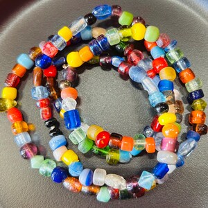 May include: A circular strand of multi-colored glass beads featuring a variety of shapes and sizes. The beads display a vibrant spectrum of colors including red, blue, yellow, green, orange, and clear tones, arranged in a continuous loop pattern.