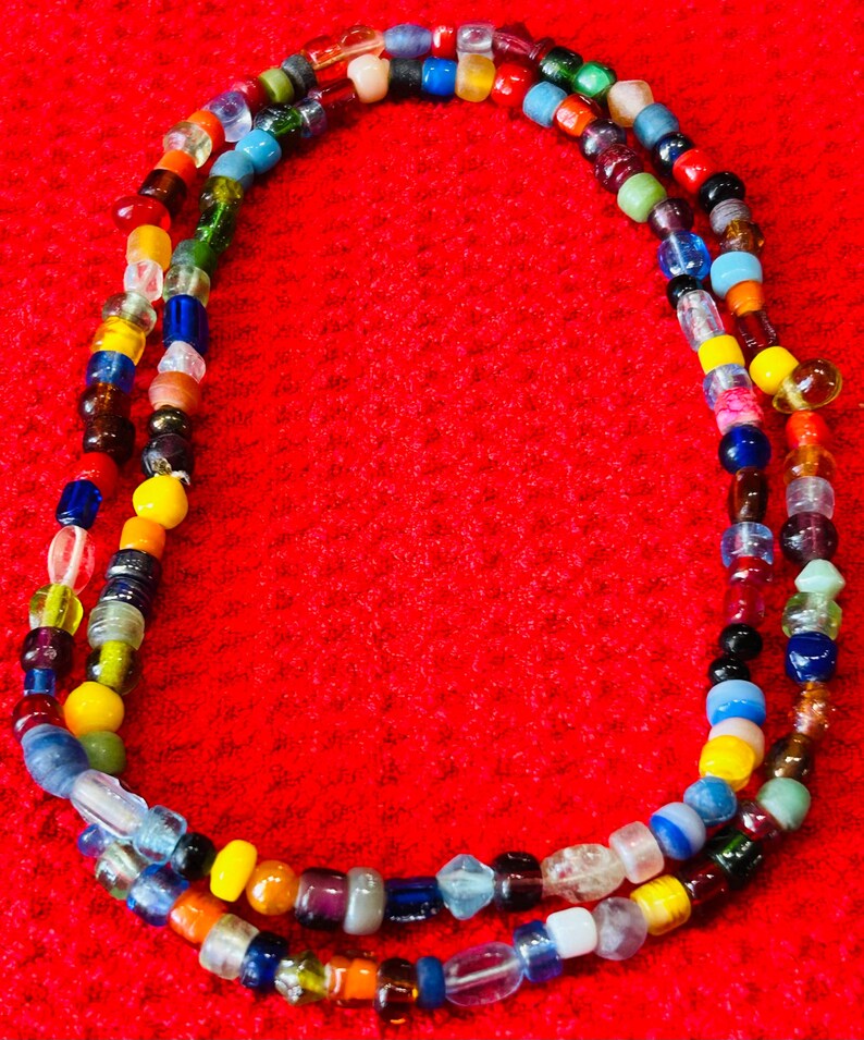 May include: A long necklace composed of a single strand of small, multi-colored glass beads. The beads feature a variety of translucent, opaque, and clear finishes in shades of blue, yellow, red, green, orange, white, black, and purple.