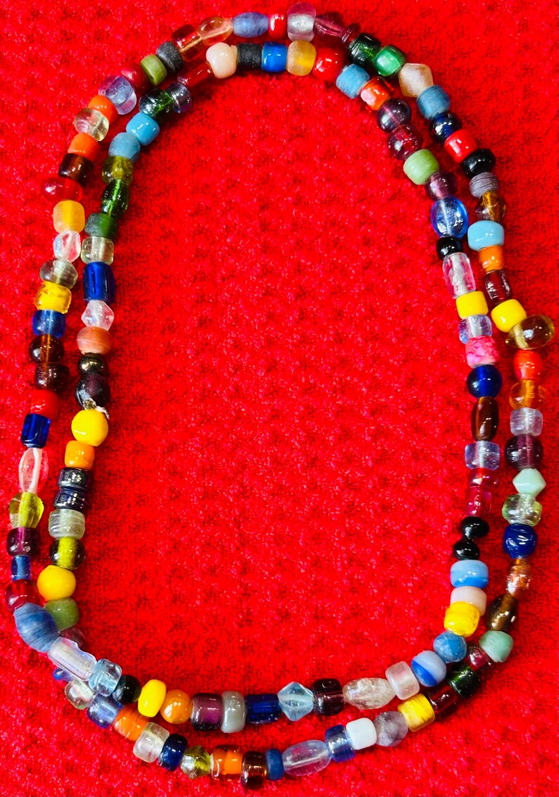 May include: A long necklace composed of a single strand of multi-colored glass beads in various shapes and sizes. The beads feature a wide spectrum of colors including red, blue, yellow, green, orange, purple, black, white, and clear glass.