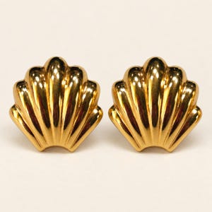 Peut inclure: Une paire de boucles d'oreilles en métal doré en forme de coquillages en éventail. Chaque boucle présente une surface polie et réfléchissante avec des stries verticales rayonnant de la base vers le bord supérieur festonné, créant un aspect symétrique.