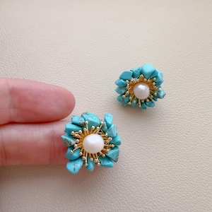 May include: A pair of turquoise and pearl earrings. Each earring features a cluster of turquoise stones surrounding a central pearl. The earrings have gold-colored accents and are designed to resemble a flower.