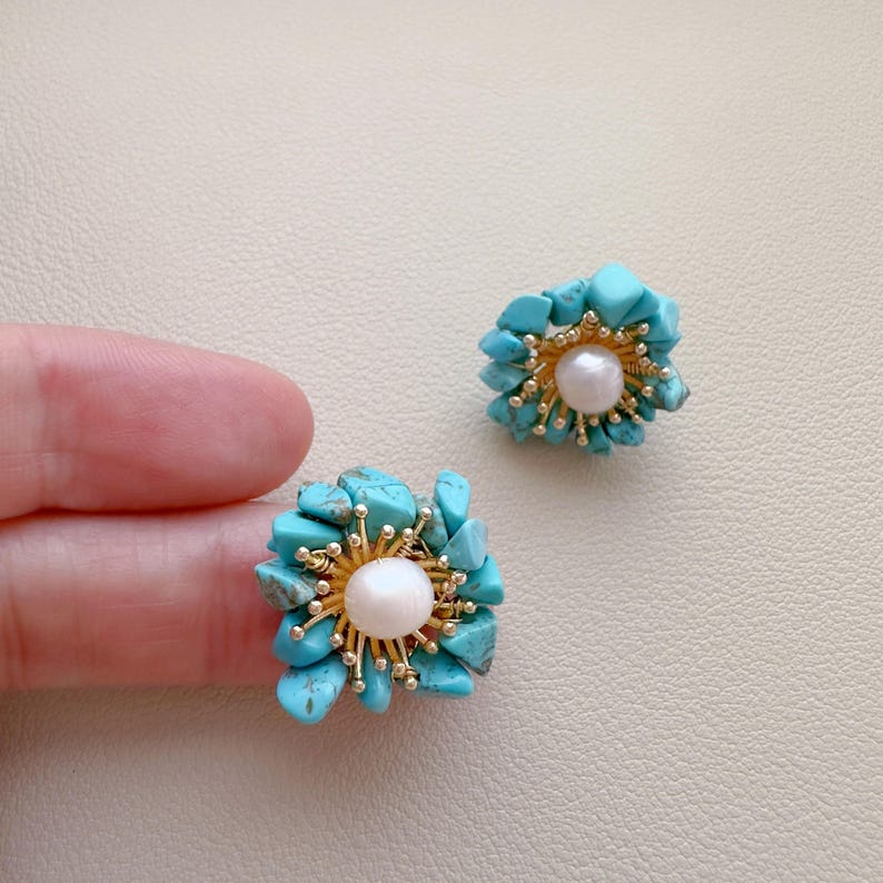 May include: A pair of turquoise and pearl earrings. Each earring features a cluster of turquoise stones surrounding a central pearl. The earrings have gold-colored accents and are designed to resemble a flower.