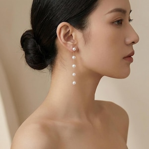May include: Elegant gold-tone earrings featuring a series of five white pearls suspended from a delicate chain. The earrings are designed to dangle, creating a graceful and sophisticated look. The pearls are round and evenly spaced.