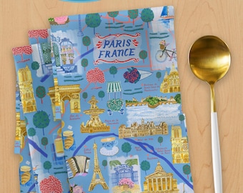 May include: A blue and white fabric napkin with a colorful illustration of landmarks in Paris, France. The napkin features the Eiffel Tower, the Arc de Triomphe, and other iconic Parisian sights. The text "Paris France" is printed in red and white.