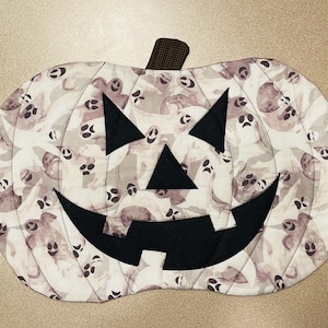 May include: A white pumpkin-shaped fabric patch with a black jack-o'-lantern face. The pumpkin is decorated with a pattern of small white ghosts.