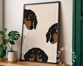 May include: Framed art print featuring three cartoon dachshund dog heads in black and brown against a cream background. The dogs are peeking out from the top and bottom of the frame. The Dawg Shop logo is in the bottom right corner.