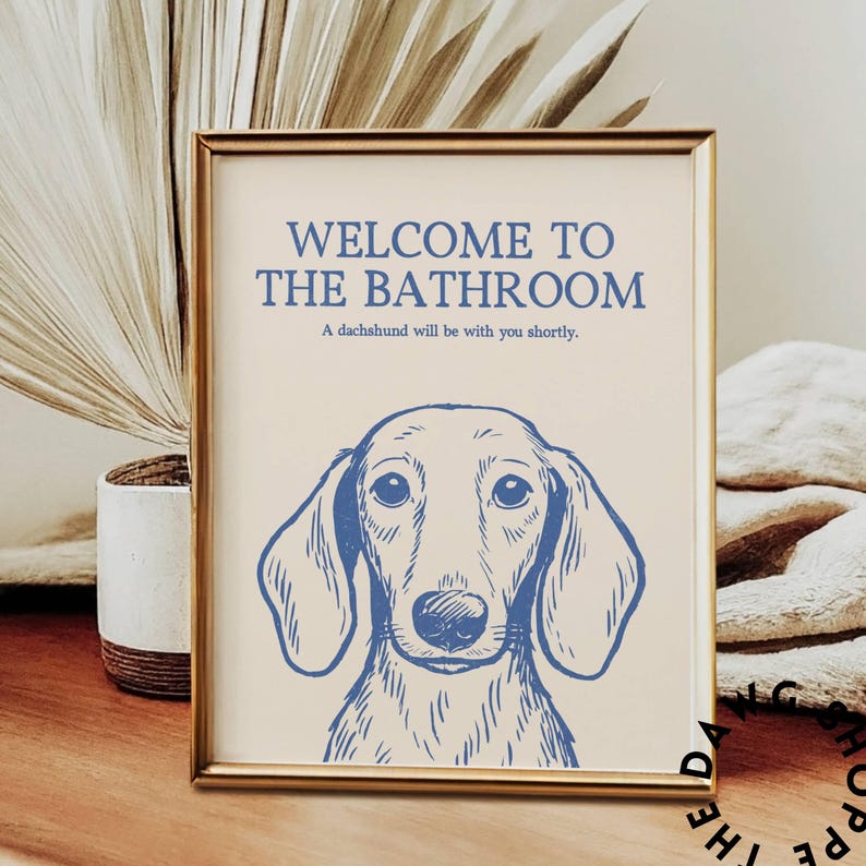 Peut inclure: Tableau encadr&eacute; avec une illustration de teckel. Le texte sur le tableau indique "WELCOME TO THE BATHROOM" et "A dachshund will be with you shortly." Le teckel est repr&eacute;sent&eacute; en bleu.