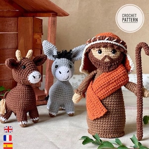 May include: A crochet pattern featuring three amigurumi figures: a brown ox with small horns, a grey donkey with a black mane, and a bearded figure wearing a head covering and orange shawl, holding a tall brown staff. Text reads CROCHET PATTERN.
