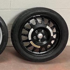 May include: A black car wheel with a tire. The wheel has a multi-spoke design and a central hub with five lug nuts. The tire is black and has a rounded profile. The wheel is likely for a car or other vehicle.