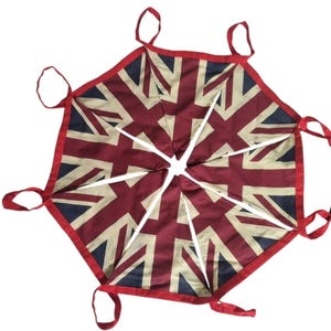 May include: A Union Jack flag bunting, featuring the red, white, and blue colours of the British flag. The bunting is made of triangular flags sewn together, with red binding and loops for hanging. The design showcases the iconic cross and stripes.