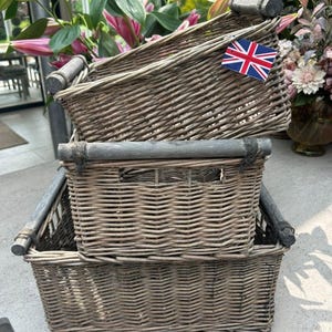 May include: Three grey woven wicker storage baskets, stacked. Each basket has a rectangular shape with rounded corners and grey wooden handles. A small Union Jack flag is attached to the top basket.